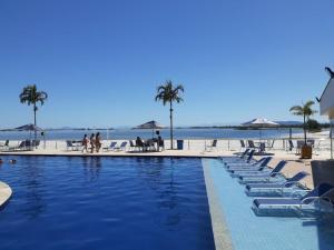 uma piscina com espreguiçadeiras e a praia em Apartamento Condomínio Golden Lake Arraial do Cabo - RJ em Arraial do Cabo