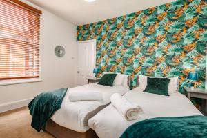 two beds in a bedroom with a tropical wallpaper at Spacious Contractor House for Large Groups - Private Parking in Northampton