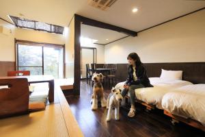 Una donna seduta su un letto con due cani di Welcome Inn SunnySteps a Shimoda