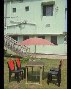 a table with chairs and an umbrella in front of a building at Vamoose Sadhana Bhaban in Sānkchi