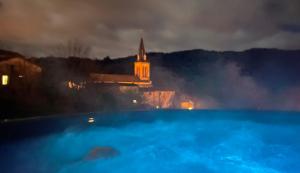 a swimming pool with a church in the background at night at Domaine de la Rue de la Tour in Valsonne