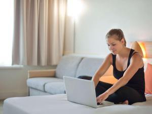 a woman sitting on a bed using a laptop computer at Novotel Porto Gaia in Vila Nova de Gaia