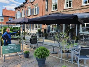 een man onder een paraplu naast tafels en stoelen bij Slapen Bij Brownies & Downies in Valkenswaard