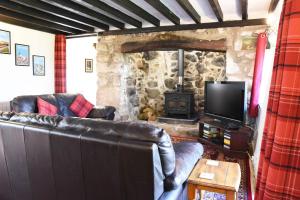 a living room with a leather couch and a stone fireplace at Ty-Gwyn Cottage in Clynnog-fawr