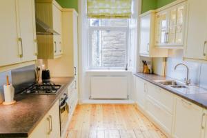uma cozinha com armários brancos, um lavatório e uma janela em Newly Furnished 2 Bedroom Apartment on Leith Walk em Edimburgo