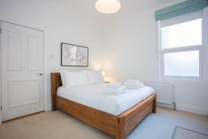 Schlafzimmer mit einem Bett mit weißer Bettwäsche und einem Fenster in der Unterkunft Stylish & Modern 3 Bed Flat in NW London with Garden in London