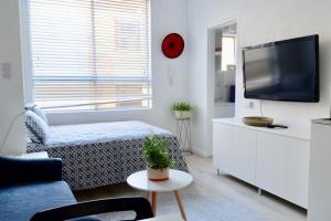 a white living room with a tv and a couch at Cute Studio Apartment in Maroubra in Sydney