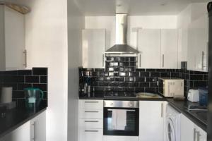 a kitchen with white cabinets and black tile on the wall at Lovely Victorian Flat for 6 in Stoke Newington in London