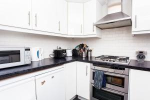 een keuken met witte kasten en een fornuis met oven bij Charming Peaceful 2 Bedroom with Parking and Garden in Londen