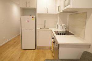 a white kitchen with a refrigerator and a sink at Modern Cosy Studio Apartment Auckland Central in Auckland