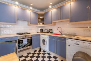 エディンバラにある2 Bedroom Apartment By Leith's Shoreのキッチン(青いキャビネット、洗濯機、乾燥機付)