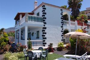 een wit huis met tafels en stoelen en een parasol bij Apartamentos Finca Casa Jardín in Tijarafe