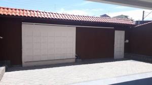 two white garage doors on a brown building at Casa com 6 quartos e confortável próxima ao Santuário in Aparecida