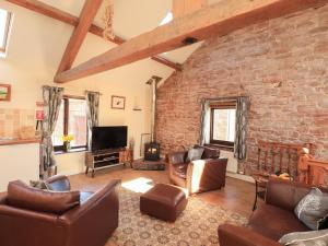 a living room with leather furniture and a brick wall at Stable Cottage in Wigton