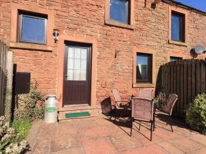 a patio with chairs and a brick building with a door at Horseshoe Cottage in Wigton