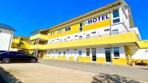 un bâtiment jaune et blanc avec une voiture garée devant dans l'établissement i-Motel, à Obertshausen