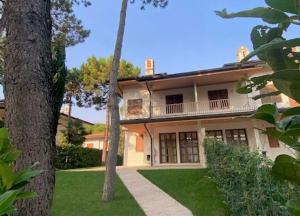 a large house with a porch and trees in front of it at Villa delle Terme in Lignano Sabbiadoro