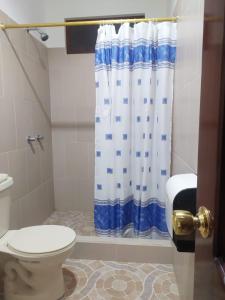 a bathroom with a toilet and a blue and white shower curtain at Hostal Los Flamencos in Puerto Villamil