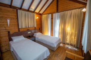 two beds in a room with wooden walls and windows at Sea Valley Lodge in Faralya