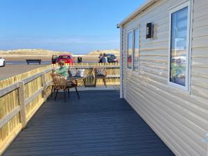 a woman sitting at a table on a boardwalk near the beach at Beachfront Lodge, Lossiemouth Bay in Lossiemouth