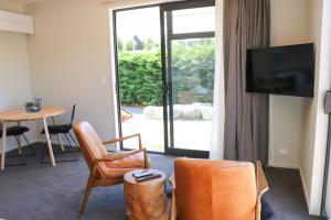 uma sala de estar com uma televisão, cadeiras e uma mesa em Fivestone Suite em Lake Tekapo