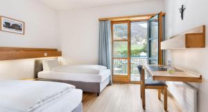 a hotel room with two beds and a desk and a window at Hotel & Bildungshaus St. Jodern in Visp