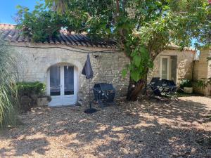 une maison en pierre avec une porte blanche et un arbre dans l'établissement Le Pressoir - Gîtes et meublés de tourisme - 2 étoiles, à Dolus-d'Oléron