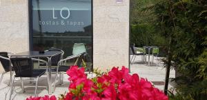 une table, des chaises et des fleurs roses devant un bâtiment dans l'établissement Pensión LO, à O Pedrouzo