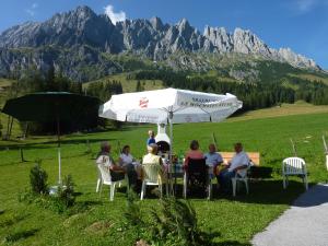 a group of people sitting at a table under an umbrella at Appartementhaus Hochkönig 1 - Wasserfall in Mühlbach am Hochkönig +5 photos