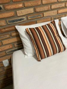 a bed with two pillows and a brick wall at Chalés Solar do Patacho in Pôrto de Pedras