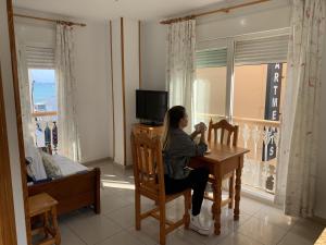 eine Frau, die an einem Tisch in einem Zimmer mit Fenster sitzt in der Unterkunft Apartamentos La Proa in Torremolinos