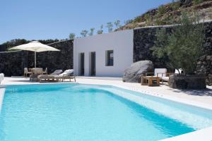 a pool with chairs and an umbrella next to a house at Aregou Villas in Imerovigli