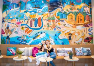 a woman sitting on a couch in front of a mural at Rove La Mer Beach, Jumeirah in Dubai