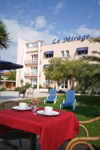 une table avec une nappe et des chaises rouges et un bâtiment dans l'établissement Cit'Hotel Le Mirage, à Istres