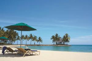 a beach with two chairs and an umbrella and the ocean at Shangri-La Tanjung Aru, Kota Kinabalu in Kota Kinabalu