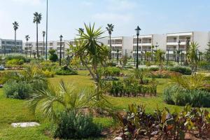 um jardim com palmeiras e plantas em frente a um edifício em Très bel appartement à OLA BLANCA em Sidi Rahal