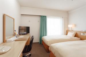 Habitación de hotel con 2 camas y escritorio con TV. en AkishimaStationHotel TOKYO, en Akishima