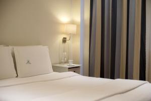1 dormitorio con 1 cama blanca con lámpara y mesa auxiliar en Piraeus City Hotel, en Pireo
