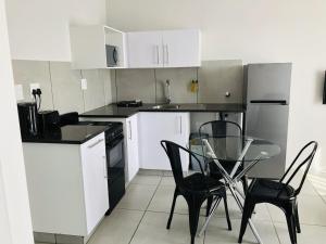 uma cozinha com armários brancos, uma mesa de vidro e cadeiras em MINT Express Sandton View em Joanesburgo