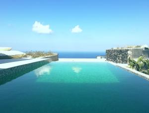 a pool of blue water with the ocean in the background at Mardanza Exclusive in Imerovigli