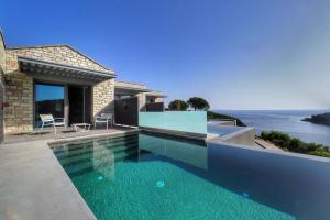 a swimming pool in front of a house with the ocean at Domotel Agios Nikolaos Suites Resort in Syvota