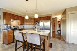 a kitchen with wooden cabinets and a island with chairs at Rodee Homestay in West Kelowna