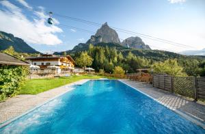 a blue swimming pool with mountains in the background at Hotel Profanter in Siusi