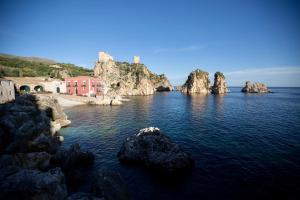 a group of rocks in the water with a red building at Le Gemme in Castellammare del Golfo