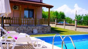 a pool with white chairs and a house with a house at Вила Марна - Villa Marna in Bŭlgarevo