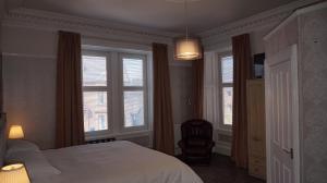 a bedroom with a bed and a chair and windows at Lindean Guest House in Dumfries