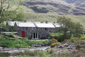 a stone house with a red door next to a river at Delphi Lodge in Leenaun