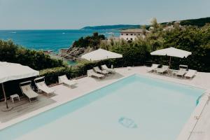 a swimming pool with chairs and umbrellas and the ocean at Villa Parisi Grand Hotel in Castiglioncello
