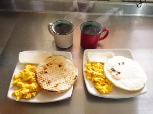 two plates of food with eggs and toast and two cups of coffee at Al Bosque Hostel & Glamping in Santa Elena
