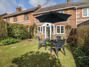 Poppy Cottage في Charlton Marshall: طاولة وكراسي مع مظلة أمام المنزل
